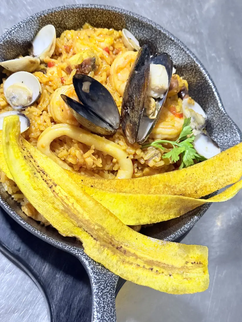 Arroz de mariscos en sartén de hierro con almejas, mejillones, calamar y tajadas de plátano